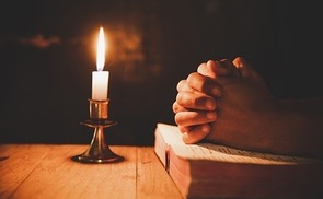 man praying on the Bible in the light candles selective focus